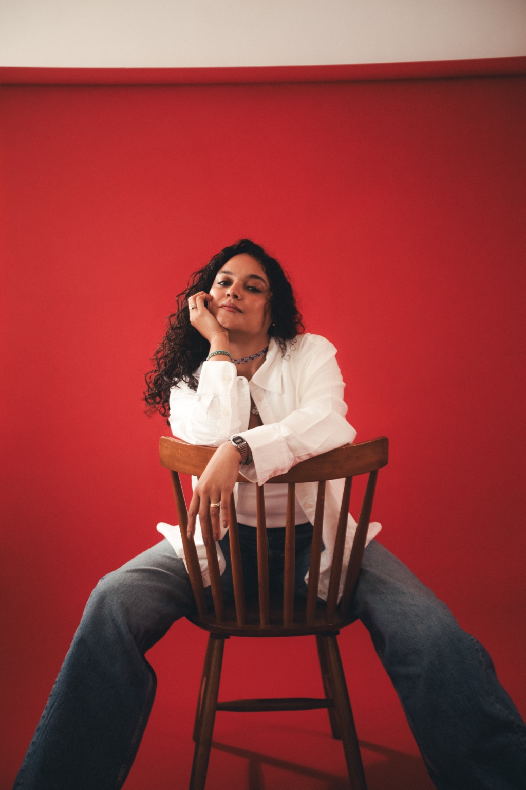 Yalfrelys Farreras seated on a wooden chair against a red backdrop